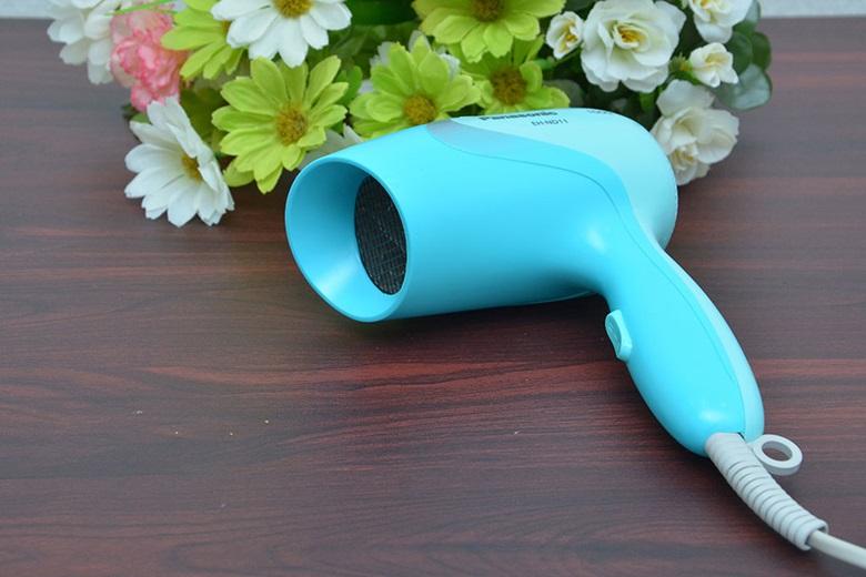 Máy sấy tóc màu xanh ngọc đặt trên bàn gỗ cạnh bó hoa nhiều màu sắc