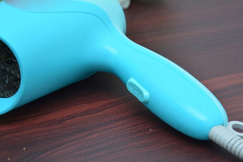 Máy sấy tóc màu xanh ngọc với công tắc trên tay cầm và dây nguồn trắng